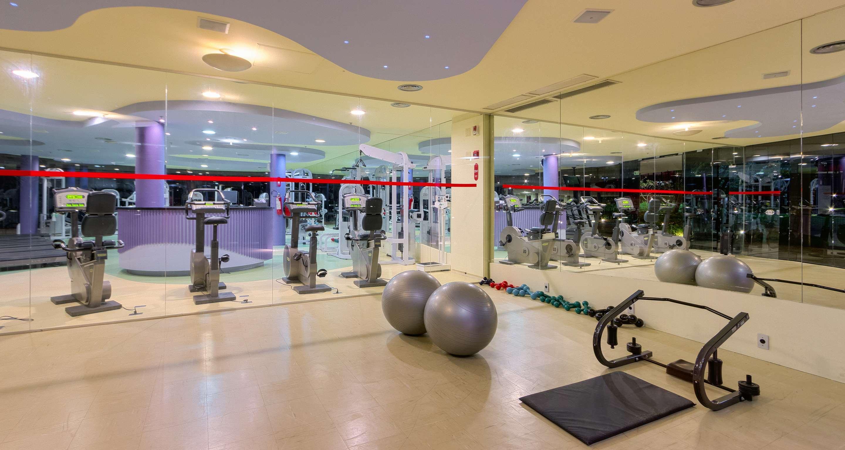 Отель Royal Tulip Brasilia Alvorada Экстерьер фото The photo depicts a gym or fitness area. In the foreground, there are two large exercise balls and a mat on the floor. Behind them, there is a wall of mirrors that reflects various gym equipment, including exercise machines and bikes. The lighting in